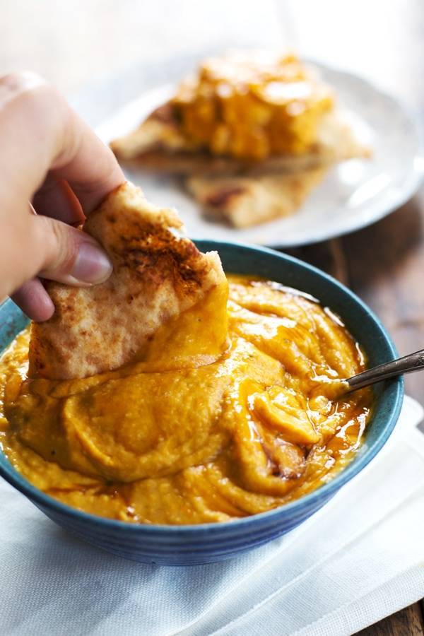 Hummus on a pita chip and in a blue bowl.